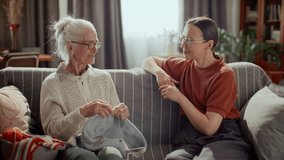 Elderly woman knitting and chatting with attentive young granddaughter sitting next to her on comfortable couch in living room at home - Powered by Shutterstock - Get 15% off with code: PIKWIZARD15