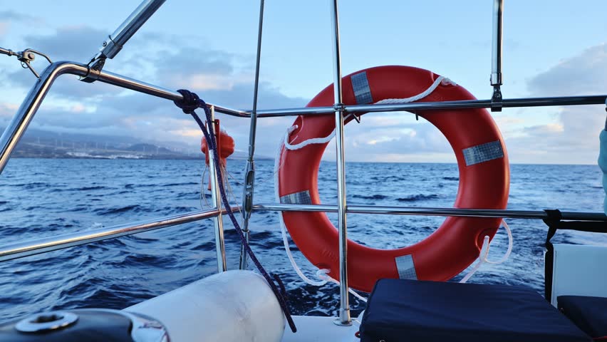 Close-up of boat railing, safety ring as ocean stretches calmly to distant shore