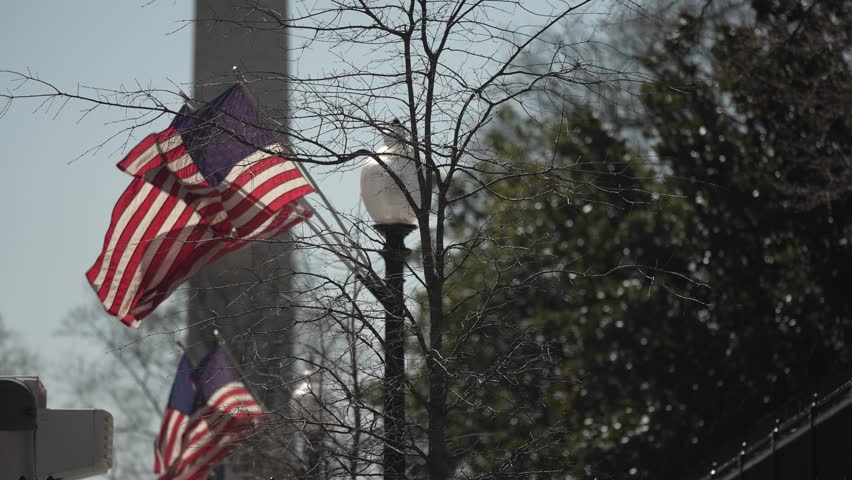 US flags on a post outside the presidents White House in Washington, DC with Washington Monument in distance.