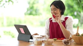 A woman is sitting at a table with a tablet and a bowl of food. She is eating a strawberry and smiling - Powered by Shutterstock - Get 15% off with code: PIKWIZARD15
