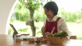 A woman is cutting vegetables on a table with a laptop in front of her. She is smiling and she is enjoying herself. The table is set with bowls of food and a laptop - Powered by Shutterstock - Get 15% off with code: PIKWIZARD15