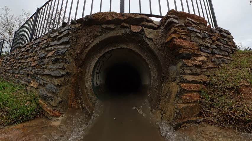 Close-Up of a Large Stone Drainage Tunnel with Water Flowing Through It After Rain, Emphasizing Stormwater Management and the Effects of Weather on Infrastructure
