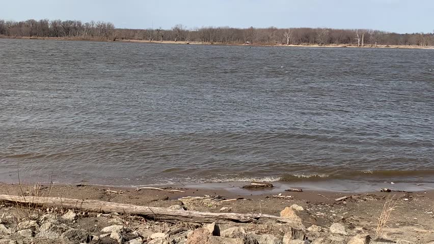 Mississippi River on a breezy early spring day lapping at the shoreline. Quad Cities Moline Illinois with Davenport Iowa on the opposite bank. Strong currents and tiny waves hitting waterway beach