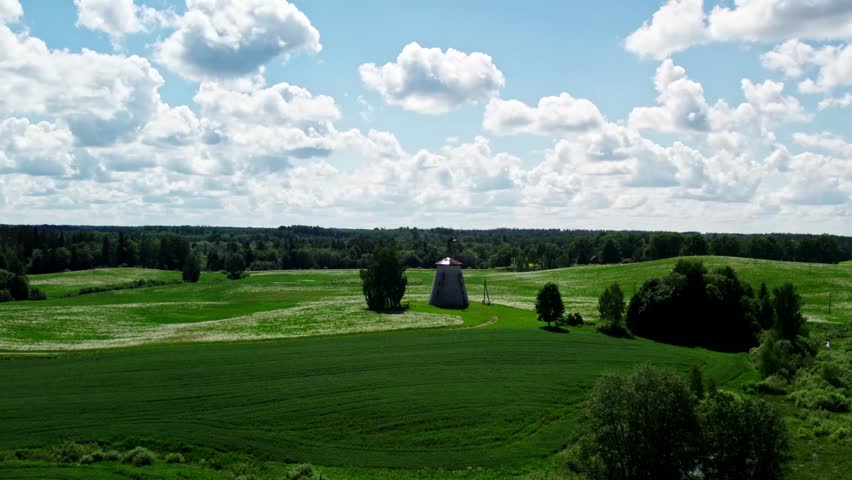 Mill in a green field. Drone shot. Beautiful landscape views. A lake is visible in the distance. Latvia