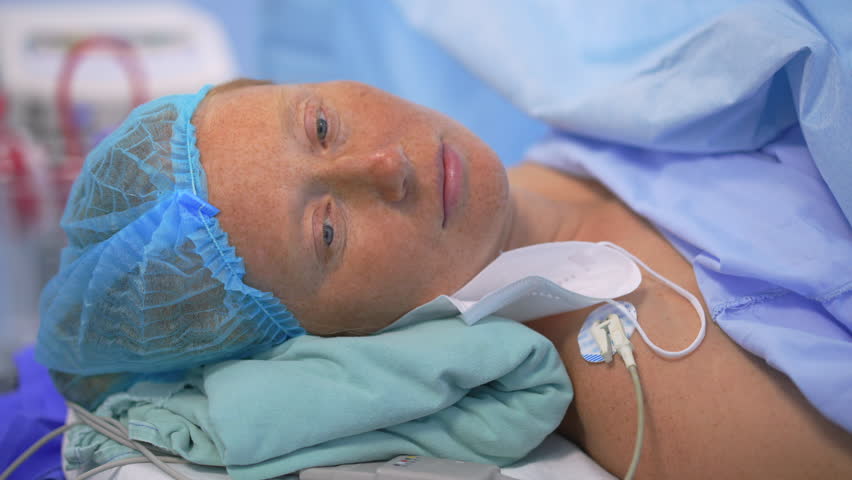 A calm woman lying on a hospital bed during a cesarean section operation. A moment of focus and medical care, highlighting childbirth, strength, and the precision of modern medical procedures.