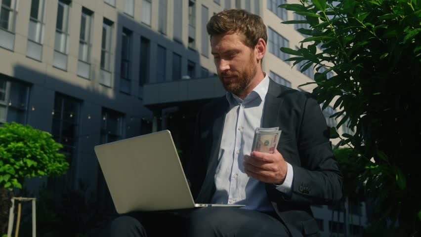 Happy rich carefree smiling wealth worker male employer with computer in city businessman business finance growth salary cash money holding counting banknotes man guy with laptop count financial prize