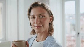 Smiling lady holding coffee in bright room portrait. Satisfied woman looking camera enjoying serene morning at home. Joyful short hair model posing with beverage cup in hands in domestic interior. - Powered by Shutterstock - Get 15% off with code: PIKWIZARD15