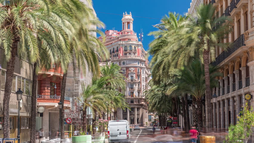 Timelapse of Banco de Valencia headquarters, historic landmark in Valencia, Spain. Stunning architecture with palm-lined street and busy traffic under a bright blue sky. Urban financial district scene