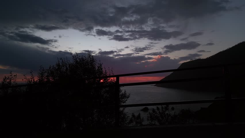 beautiful scenic epic drone flight over the sea at sunset with the red sun setting into the sea on the horizon with a colorful sky full of gray clouds in Framura Italy Liguria landscape 