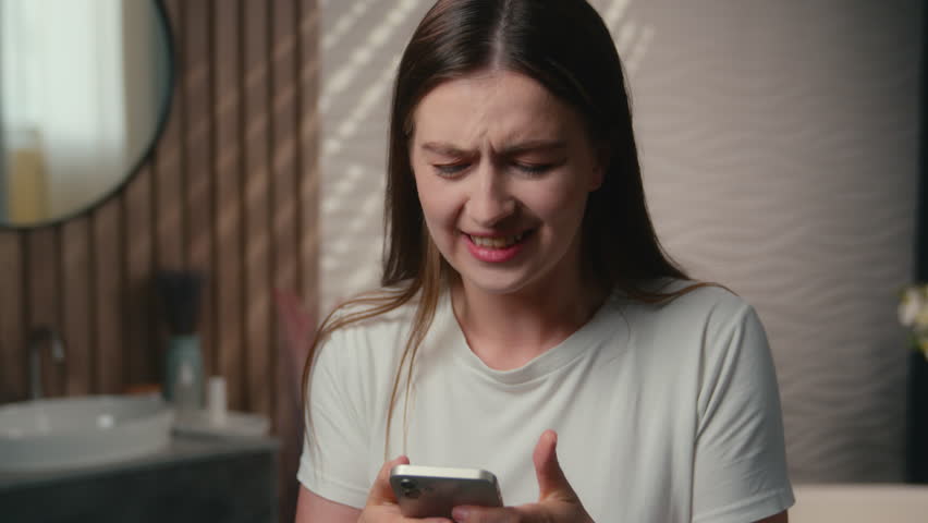 Caucasian woman addict gadget female customer stressed girl internet addiction gambling smartphone play game scrolling mobile phone worried upset anxious shopping sales problem bad news in bathroom