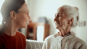 Elderly woman smiling and talking to young granddaughter, enjoying warm conversation on couch in living room filled with bright sunlight - Powered by Shutterstock - Get 15% off with code: PIKWIZARD15