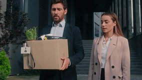 Two business people leaving office in city Caucasian sad man businessman fired male guy lost job holding dismissal box with staff woman HR recruiter businesswoman support calming female friendship - Powered by Shutterstock - Get 15% off with code: PIKWIZARD15