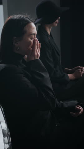 Vertical shot of young woman in black unable to manage her emotions during solemn funeral service