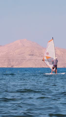 Man learns to ride on a board with a sail, windsurfing. windsurfing on the crystal clear water