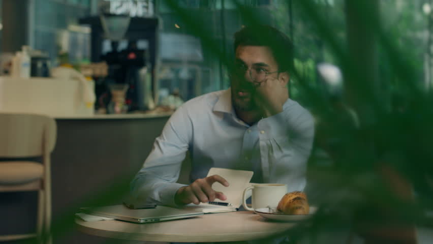 Bored sad business man Indian Arabian guy male employee freelance worker tired businessman exhausted weary student lack sleep insomnia yawn drink morning coffee surging energy write study work in cafe