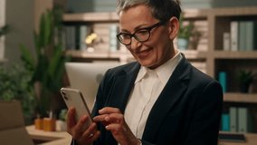 In office happy smiling old Caucasian woman business female businesswoman mature senior employer middle-aged CEO entrepreneur using mobile phone social media smartphone amazed surprised wonder app - Powered by Shutterstock - Get 15% off with code: PIKWIZARD15