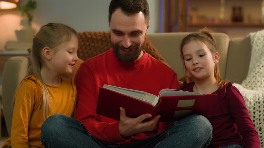 Caucasian family happy kids little girls daughters father talk laugh sit at home evening loving parent read book night fairy tale children dad reading learning textbook watching photo album together