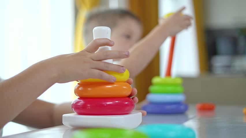 Brother sister play with pyramid toy. Brother sister stacking rings on pyramid. Brother sister focused on pyramid toy. Early childhood play with educational toy. Bonding through pyramid toy play.