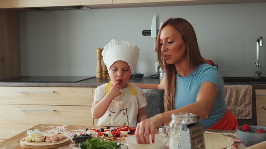 Funny family daughter and mother making pizza for dinner at the kitchen. Happy family together.