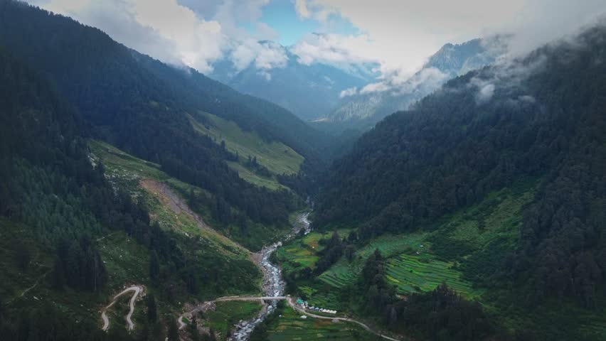 beautiful ariel shot over the mountain valley with glacial river flowing swiftly and mountains are covered with monsoon vegetation and pine trees in the mountains