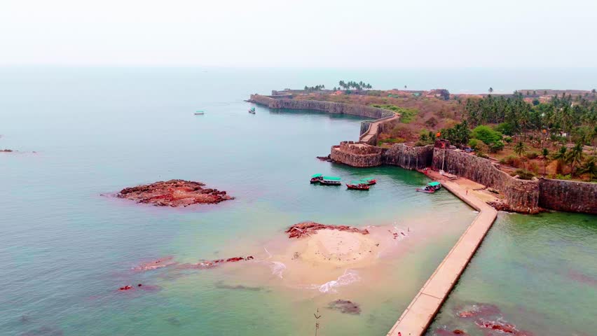 Drone View of Island with Palm Trees and Shelter, Aerial Shot Shows Fort by Calm Ocean, Coastal Fortress Stands Near Sandy Edge, Fishing Boats Dock Beside Historic Landmark, Vessels sail in Sea Water
