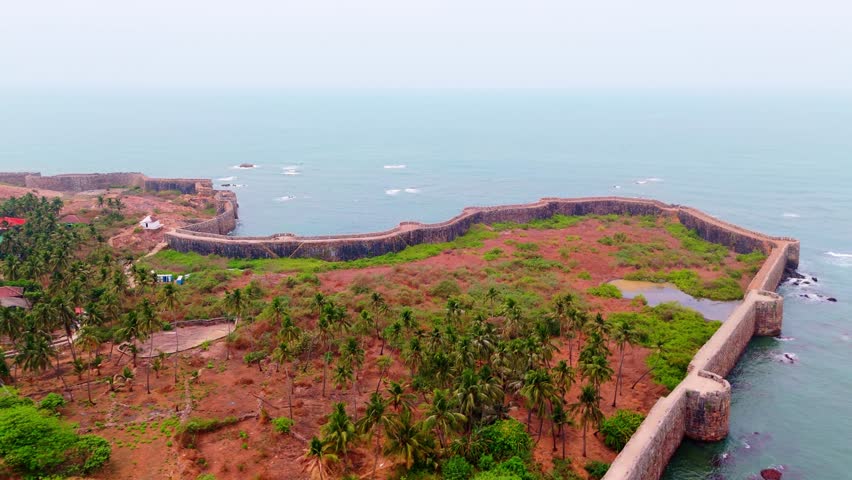 Aerial Shot Shows Fort by Calm Ocean, Drone View of Island with Palm Trees and Shelter, Coastal Fortress Stands Near Sandy Edge, Fishing Boats Dock Beside Historic Landmark, Vessels sail in Sea Water