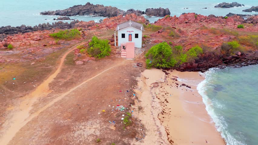 Aerial view spots white cottage on craggy shore, Drone shot House stands beside rough cliffs and green land, Seaside bluff holds lone home with slant roof, Coastal highlights building near crag, Steps