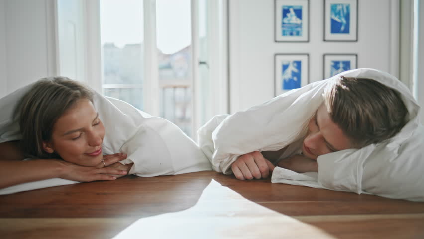 Tender lovers touching hands in sunlight closeup. Playful couple lying under blanket enjoying intimate moment at home. Affectionate man woman cozy relaxed atmosphere. Bonding relationship concept