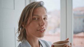 Closeup woman drinking breakfast coffee by home window. Satisfied lady tasting beverage enjoying tranquil morning atmosphere indoors. Serene smiling girl looking camera with cup feeling content.  - Powered by Shutterstock - Get 15% off with code: PIKWIZARD15