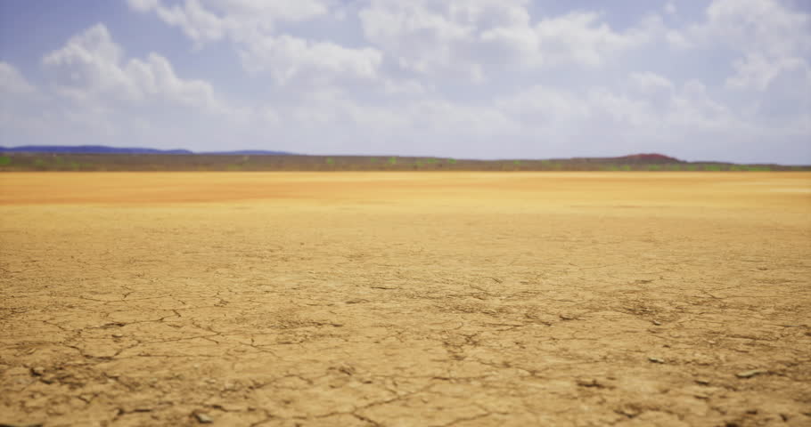 Barren land stretches for miles, showcasing cracked dry earth under a bright sky filled with fluffy clouds. The landscape hints at arid conditions and a lack of moisture.