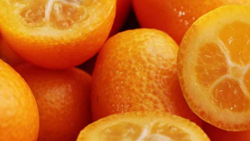 Ripe kumquats with vibrant green leaves receiving fresh water droplets, showcasing natural citrus fruit freshness on rustic wooden surface