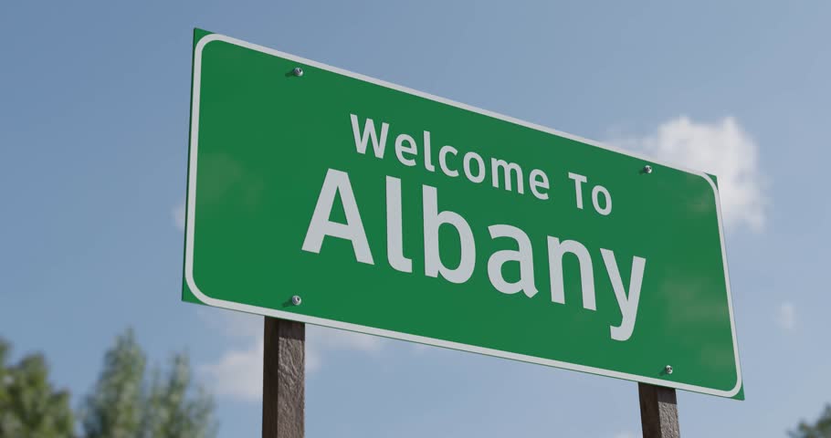 Driving By A Welcome To Albany, New York Green Road Sign Against a Blue Sky and Clouds - United States Capital Series.