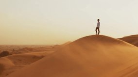 Young happy male person stands  on the sand hill in the desert and looking to sun, profile view. Young man in stylish clothes stands alone  in sand dunes in the desert at sunset.  Freedom concept. - Powered by Shutterstock - Get 15% off with code: PIKWIZARD15