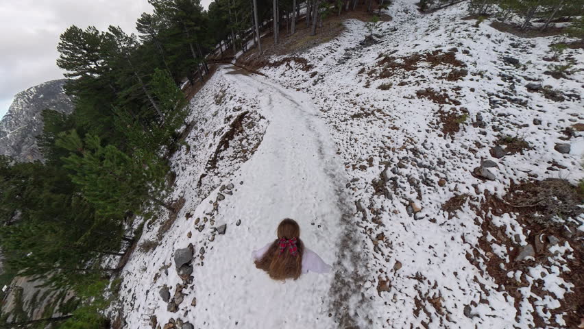 Woman walking down a snowy forest trail with surrounding pine trees, heading toward a distant mountain view under a bright sky with scattered clouds. Scenic Winter Walk