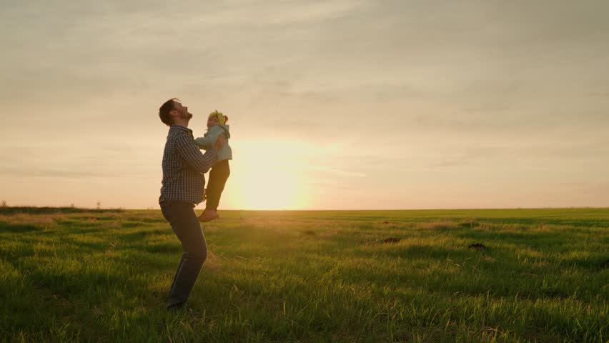 Dad throws happy daughter up in air with his hands in sun rays. Father, little child play and rejoice together. Happy family weekend in nature. Child in parent arms. Happy family concept. Green field