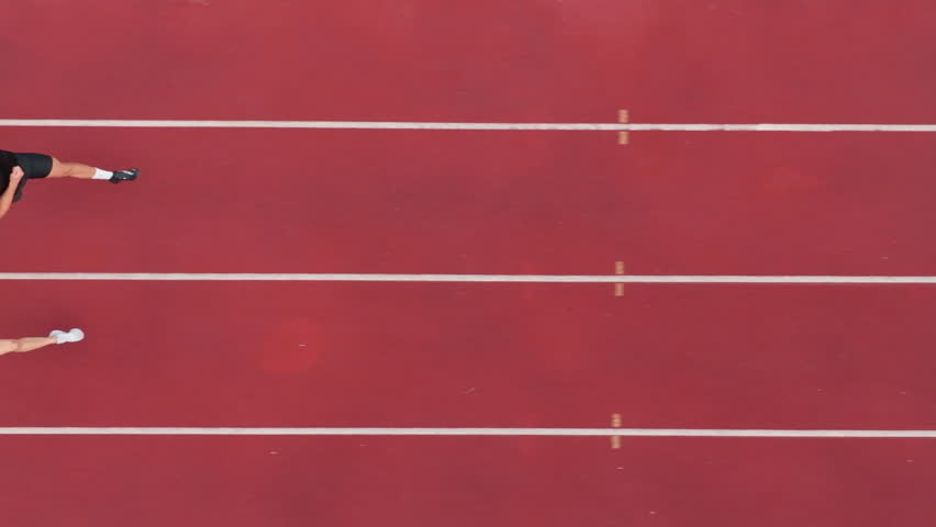Aerial drone shot from above of an athletic couple jogging side by side on a stadium track, captured in slow motion, emphasizing their fitness, rhythm, and energy as they move in perfect sync