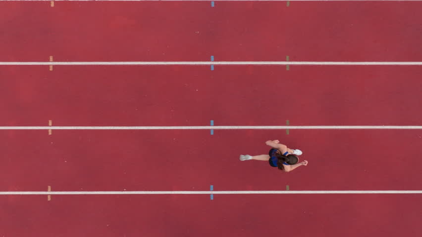 Top down view aerial drone shot of a professional female athlete sprinting on a large stadium athletics track. Dynamic slow motion cinematic footage captures her power, speed, and determination in - Powered by Shutterstock - Get 15% off with code: PIKWIZARD15