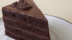 A sliding close-up shot of a rich chocolate cake on a white plate with a black rim, moving smoothly from left to right against a beige background. Perfect vertical stock video for dessert visuals. - Powered by Shutterstock - Get 15% off with code: PIKWIZARD15