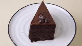 A rich chocolate cake rotates on a white plate with a black rim against a beige background. Smooth motion highlights texture and detail. Perfect vertical stock video for dessert and bakery visuals. - Powered by Shutterstock - Get 15% off with code: PIKWIZARD15