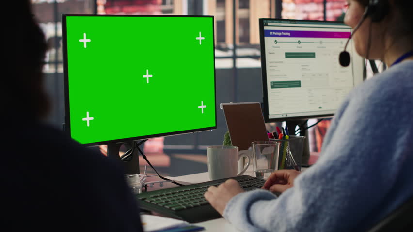 Call center employee working on green screen mockup PC, doing account management in office. Customer support agent in front of chroma key isolated screen computer handling calls, camera A close up