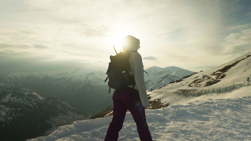 Hiker walking confidently on a snowy slope at sunset. Slow motion
