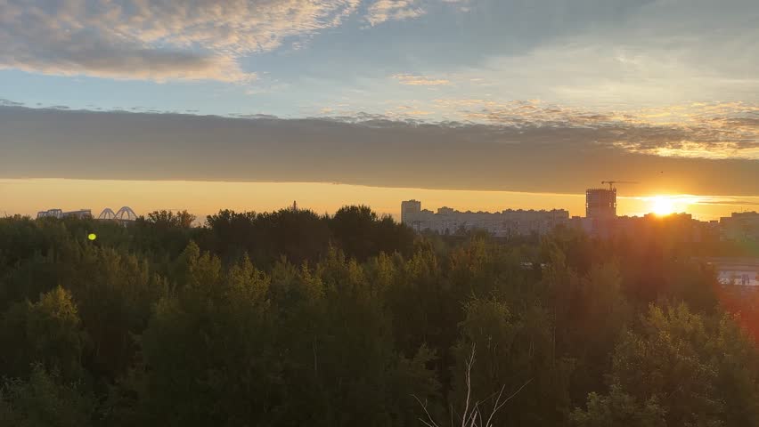 A beautiful sunset over a city with a large building in the background. The sky is filled with clouds and the sun is setting, creating a warm and peaceful atmosphere
