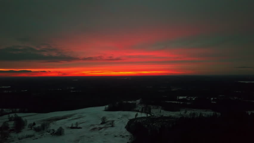 Aerial view of a vivid red and orange sunset over a snowy winter landscape in Latvia during the evening