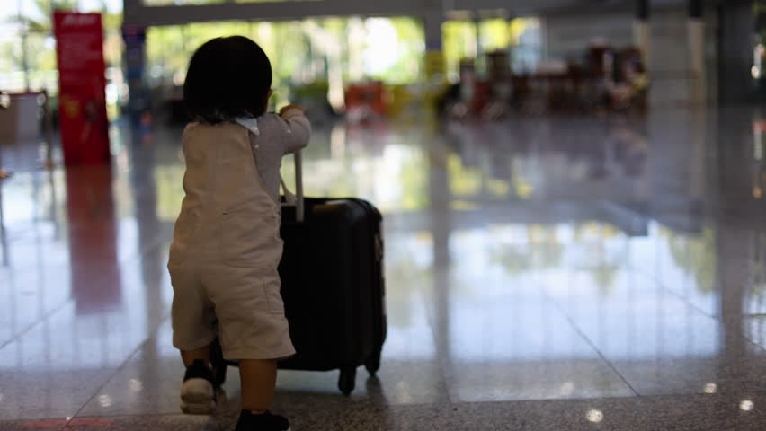 Little boy with suitcase travel in busy airport.  The traveler runs with his suitcase