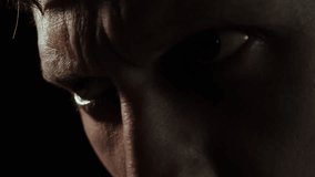 Intense close-up of a man's furrowed brow and piercing gaze, expressing anger, tension, and determination in dramatic low-light - Powered by Shutterstock - Get 15% off with code: PIKWIZARD15