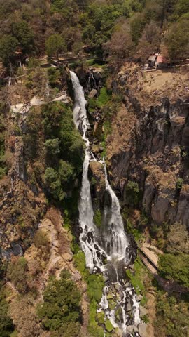 A vertical view of a stunning waterfall flowing between lush green cliffs on a mountain.