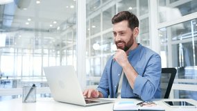 A smiling businessman working on a laptop sitting at a workplace in business office. Handsome bearded male worker typing on computer, banking, texting a client, chatting online or busy with a project - Powered by Shutterstock - Get 15% off with code: PIKWIZARD15