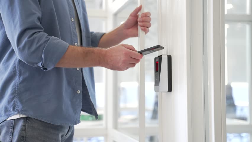 Close up of businessman unlocking door using mobile phone application. Unlocks a modern glass white office. Scanning open smartphone with mock up screen app. Smart electronic locks with keyless access