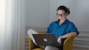 A young woman is working on a laptop while sitting in an armchair in the living room - Powered by Shutterstock - Get 15% off with code: PIKWIZARD15