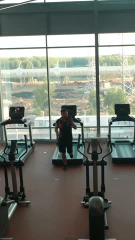 Aerial footage in the gym. The man saying goodbye and high five to his friends after running on a treadmill and leaving exercise room. Vertical shot.